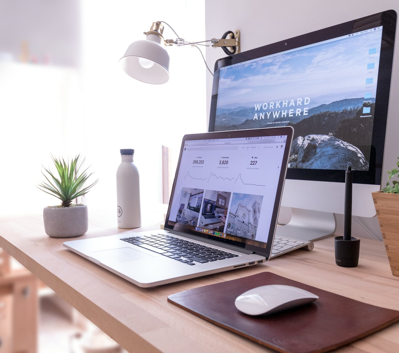 A tidy workspace with a laptop and monitor on a pale wooden desk