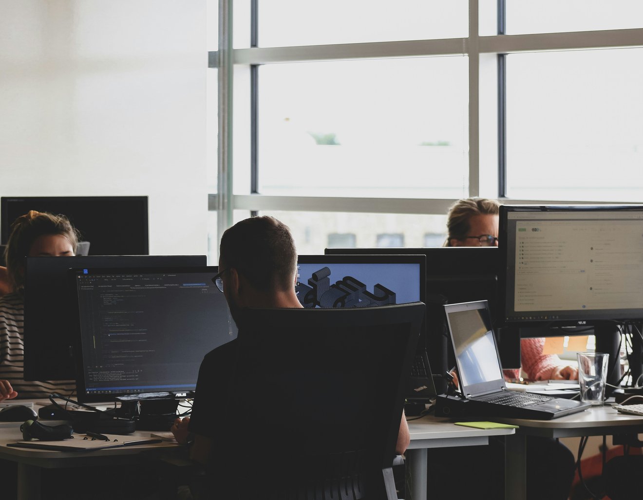 A room of people working at desks in front of monitors