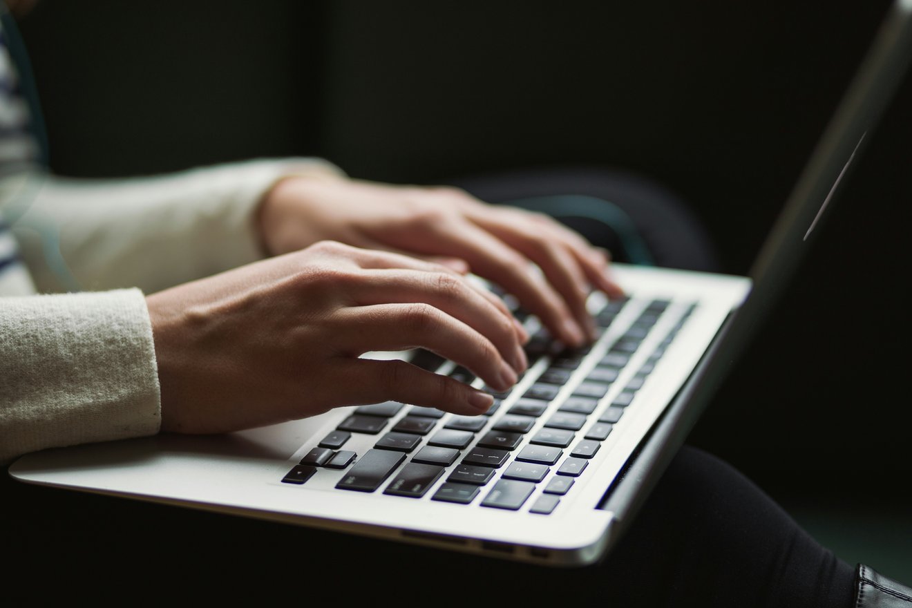 Hands typing at a laptop keyboard while drafting a document